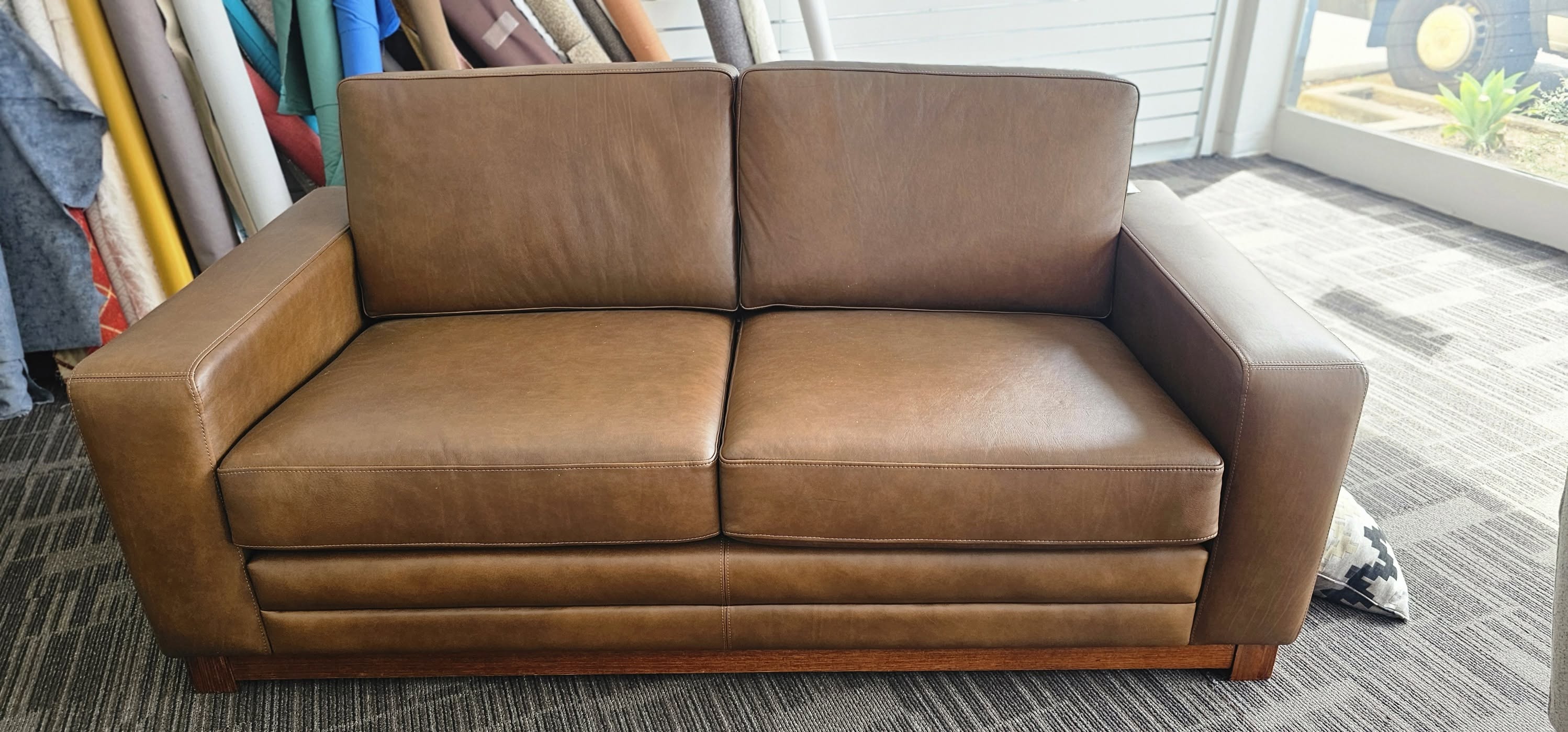 Tan leather two-seater sofa with stitched cushions on a timber base